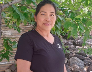 woman with black hair pulled back and a black shirt in front of a tree