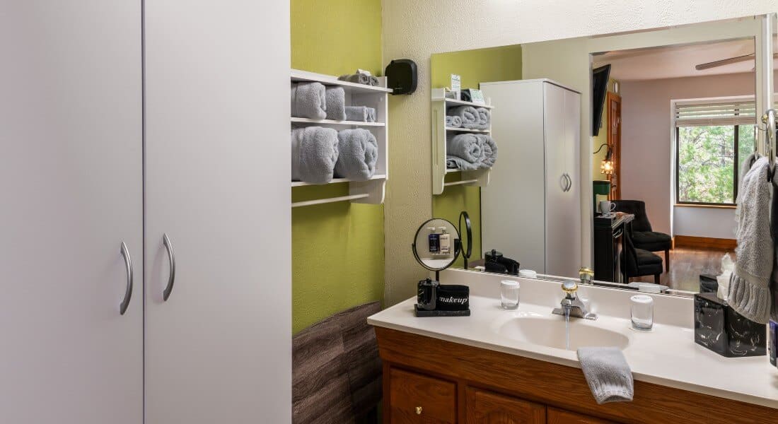 view of bathroom with green wall, gray towels, vanity, mirror and armoire 