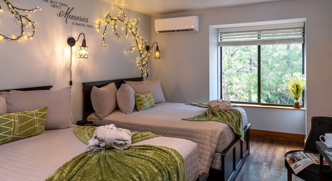 view of guest room with window from bathroom. 2 double beds with gray linens and green decorative pillow and blankets