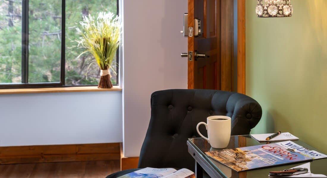 black chair next to small brown desk with cup of coffee near guest room door with picture window ahead