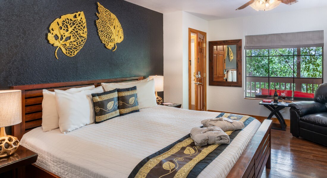 view of king bed from the bathroom door, overlooking large picture window. Bed with white linens and black/gold bed decor